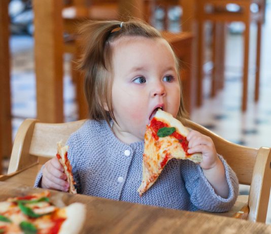 Kleines Mädchen isst ein großes Stück Pizza