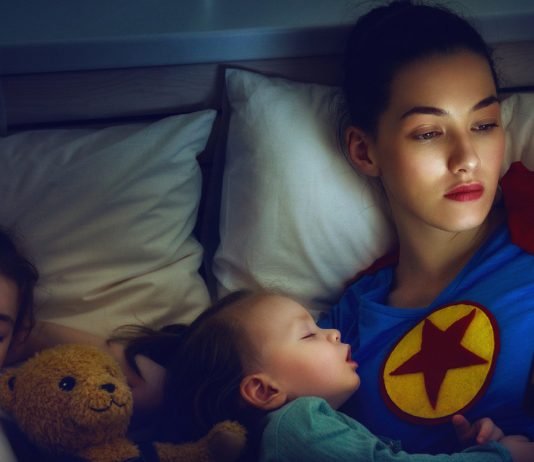 Superhelden Mama liegt mit ihren Kindern im Bett