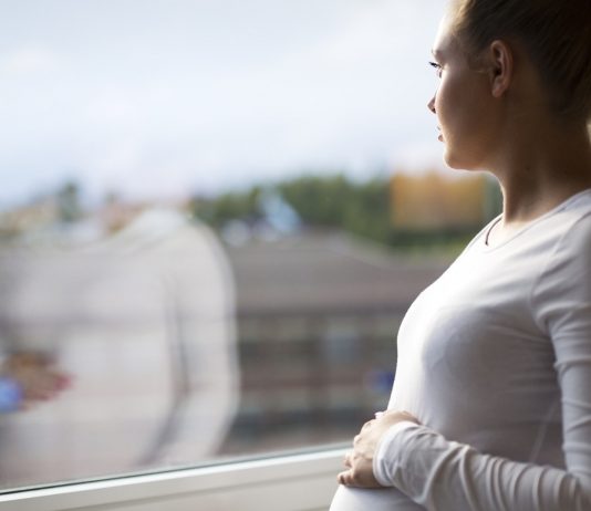 Schwangerschafts-Depression: Wann tritt sie auf: Schwangere Frau schaut aus dem Fenster