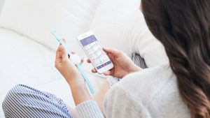 Frau hält Ava Armband und Smartphone mit App