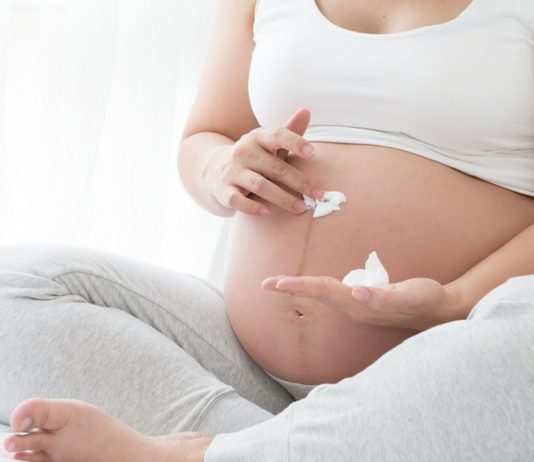 Schwangere Frau cremt sich den Bauch ein
