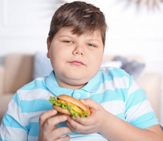 übergewichtiger Junge mit Burger in der Hand