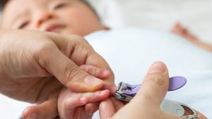 Mutter schneidet Baby die Fingernaegel mit einem Nagelknipser