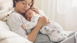 Kaiserschnittnarbe pflegen: Mama in bequemer Kleidung mit Baby im Bett sitzend