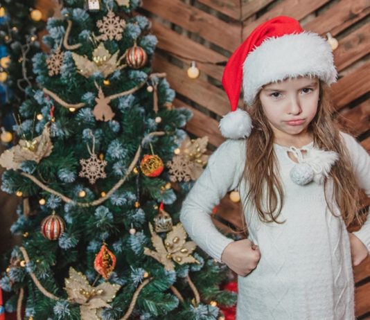 Enttaeuschtes Maedchen vor dem Weihnachtsbaum möchte Weihnachtsgeschenke tauschen