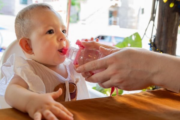 Mutter gibt Kind die Flasche mit Tee fuer Babys