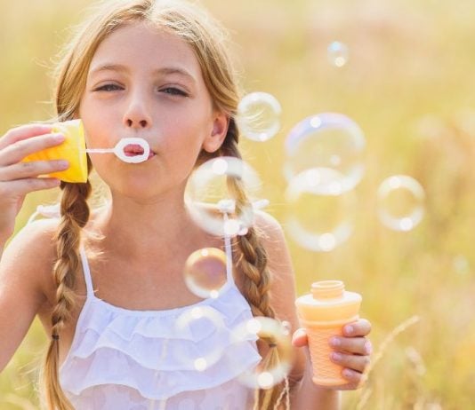 Auf diesem Bild ist ein Mädchen im Sommer zu sehen, das Seifenblasen produziert.
