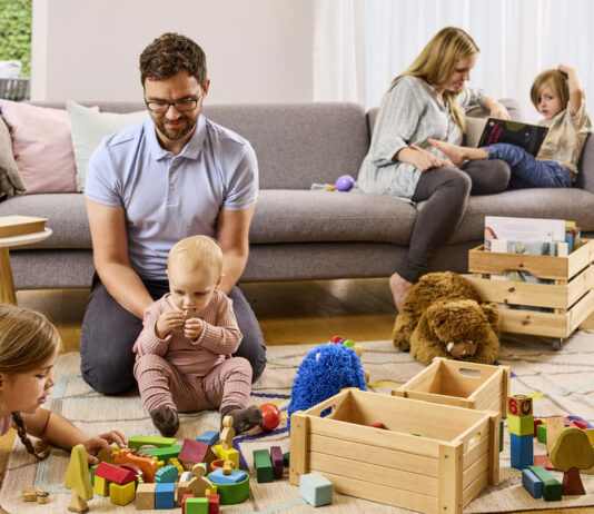 Eine Familie mit drei Kindern spielt im Wohnzimmer und genießt die gemeinsame Zeit.