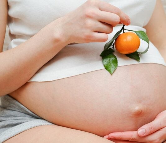 Auf diesem Bild ist eine Schwangere zu sehen, die eine Mandarine in der Hand hält.