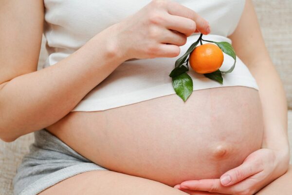 Auf diesem Bild ist eine Schwangere zu sehen, die eine Mandarine in der Hand hält.