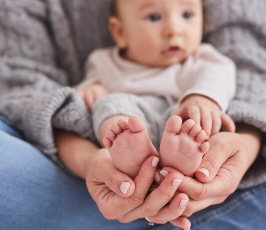 Mama hat Baby auf dem Schoß und hält die Babyfüße fest.