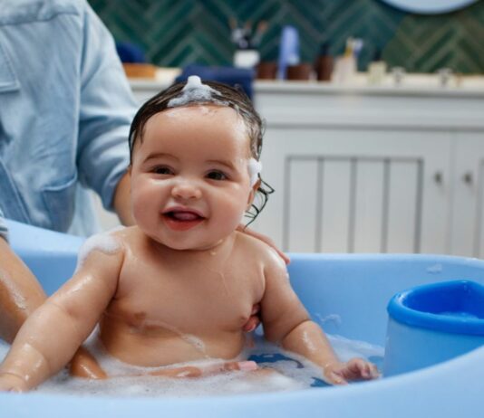 Ein fröhliches Baby wird von seiner Mutter in einer Badewanne gebadet.