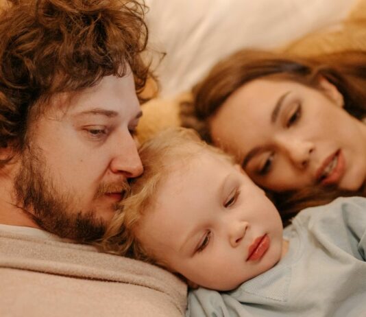 Eltern kuscheln mit Kind als Abendroutine vor dem Schlafengehen