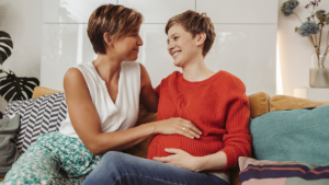 Schwangere und Freundin sitzen auf dem Sofa und Lachen