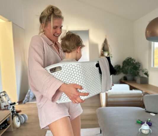 Mama trägt ihr Kind im Wäschekorb, beide lachen dabei und haben Spaß.
