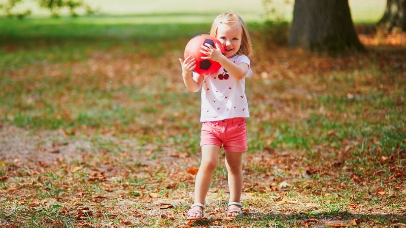 Kleines Mädchen spielt mit einem Ball im Park