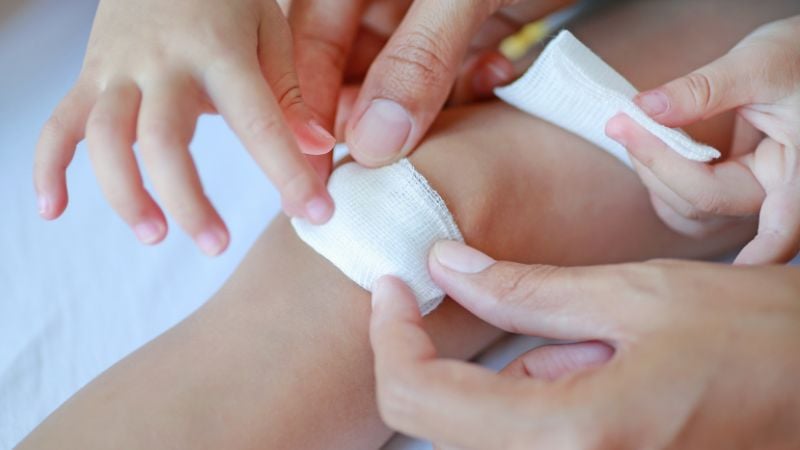 Eine Wunde am Knie von einem Kind wird mit einem Pflaster versorgt.