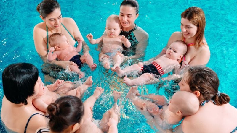 Eine Gruppe von Müttern übt mit ihren Babys das Strampeln im Wasser beim Babyschwimmen.