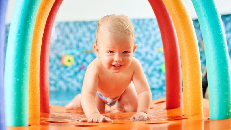 Baby krabbelt auf einer bunten Krabbelmatte beim Babyschwimmen.