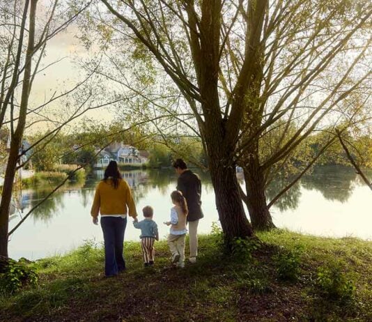 Familie steht gemeinsam zwischen Bäumen an einem See.