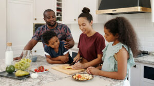 Familie steht gemeinsam in der Küche und kocht und isst.