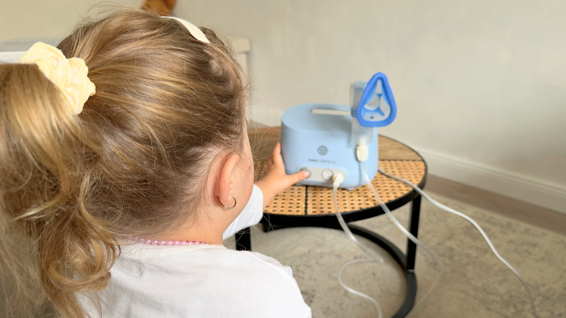 Kleines Mädchen schaltet das Inhalationsgerät PARI Compact2 selbständig ein.