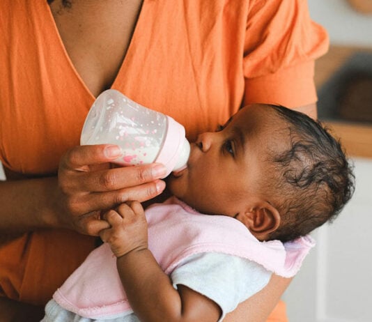 Mama füttert Baby auf dem Arm mit der Flasche.