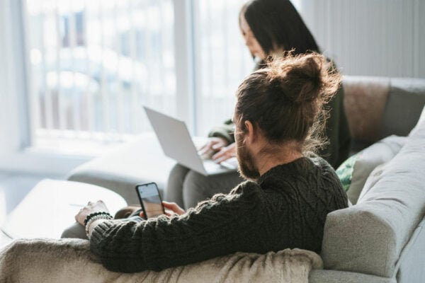 Frau und Mann sitzen auf der Couch. Sie schaut auf den Laptop. Er schaut aufs Handy.