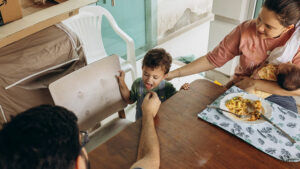 Eltern füttern Kind, das am Esstisch steht. 