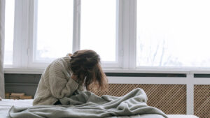 Frau vergräbt im Bett sitzend die Hände im Gesicht.