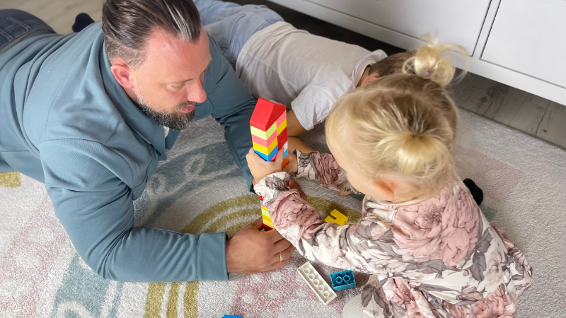 Papa hilft seiner kleinen Tochter dabei, einen Turm aus Bausteinen zu bauen.
