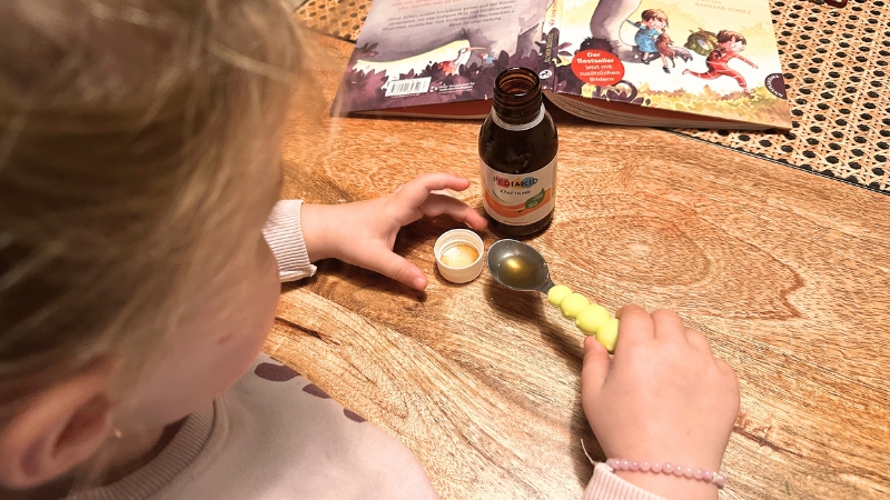 Ein kleines Mädchen macht sich das Kraftkind Sirup von Pediakid auf den Löffel.