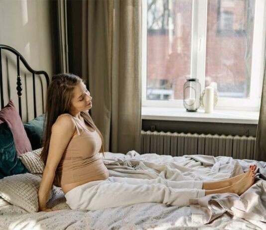 Schwangere Frau sitzt auf ihrem Bett.