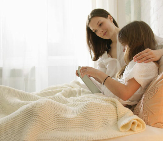 Mädchen sitzt im Bett und wird von Mutter umarmt.