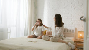Mädchen sitzt auf dem Bett und trinkt Wasser, die Mama sitzt daneben.