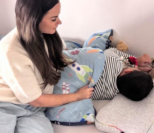 Mama deckt ihren schlafenden Sohn mit einer Decke zu.