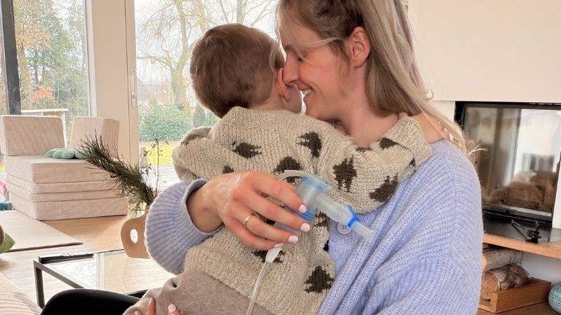 Mama und Kleinkind kuscheln, während Mama das Inhalationsgerät in der Hand hält.